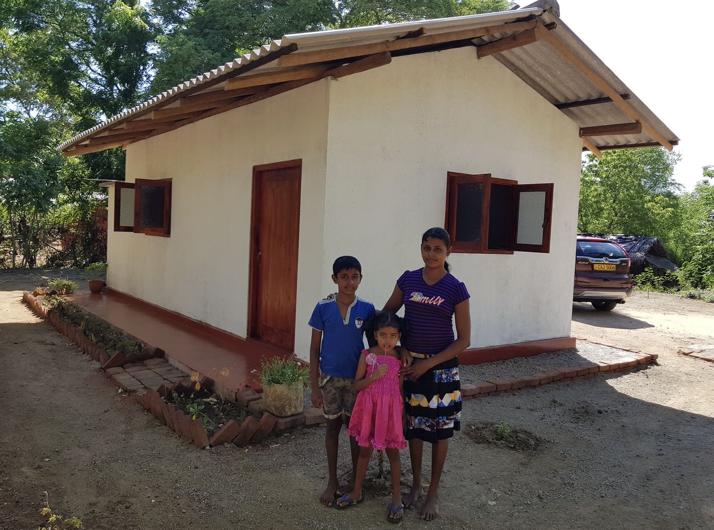 A mother and her two children stand proudly in front of their newly built home with white walls and timber windows