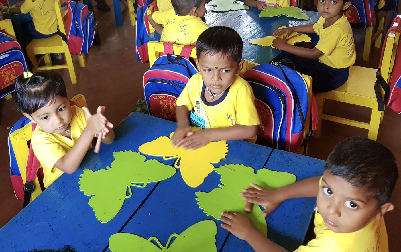 Preschool children in yellow Light a Life t-shirts play with butterfly puzzles at bright blue classroom tables