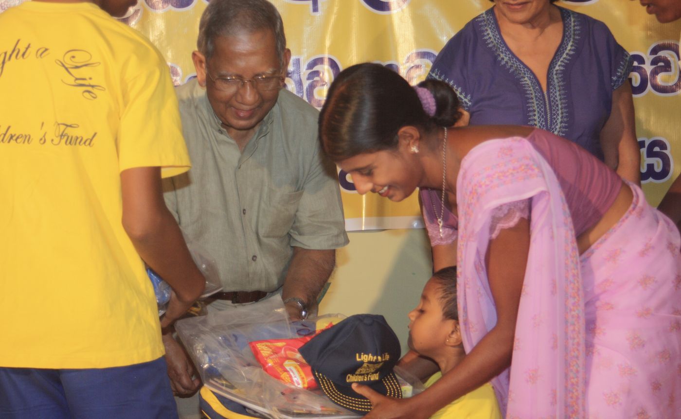 Trustees hand a Light a Life cap and a parcel of school supplies to a smiling young scholarship student