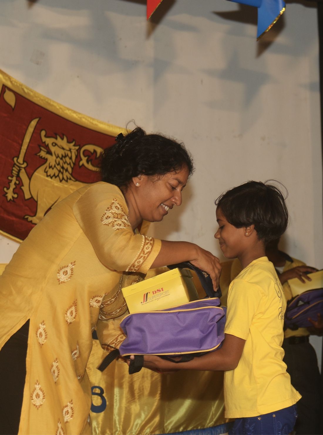 A volunteer smiles as she hands a school backpack and new shoes to a young girl at a Light a Life ceremony